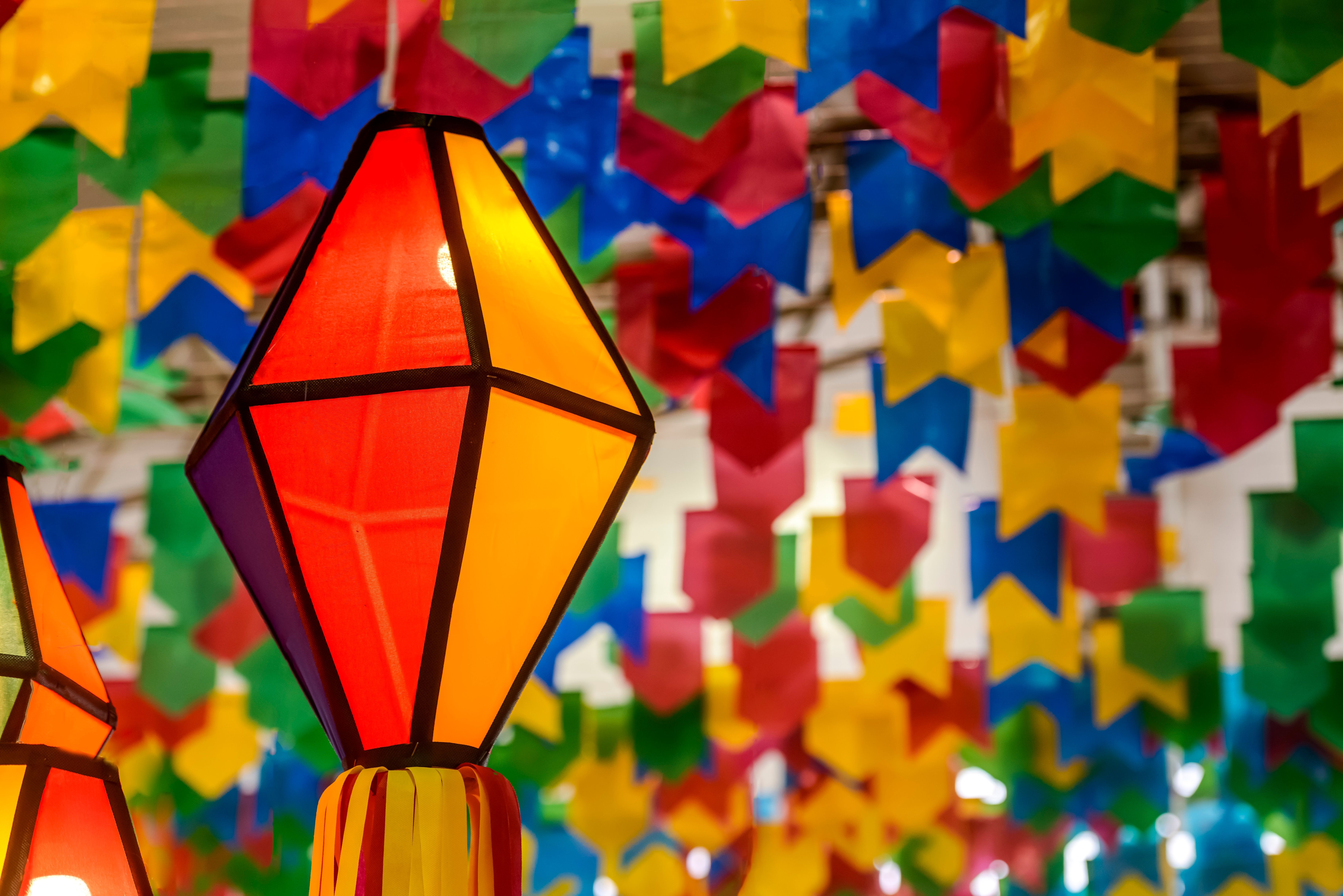 Imagem de decoração de festa junina com um balão colorido e ao fundo diversas bandeirinhas azuis, vermelhas e amarelas.